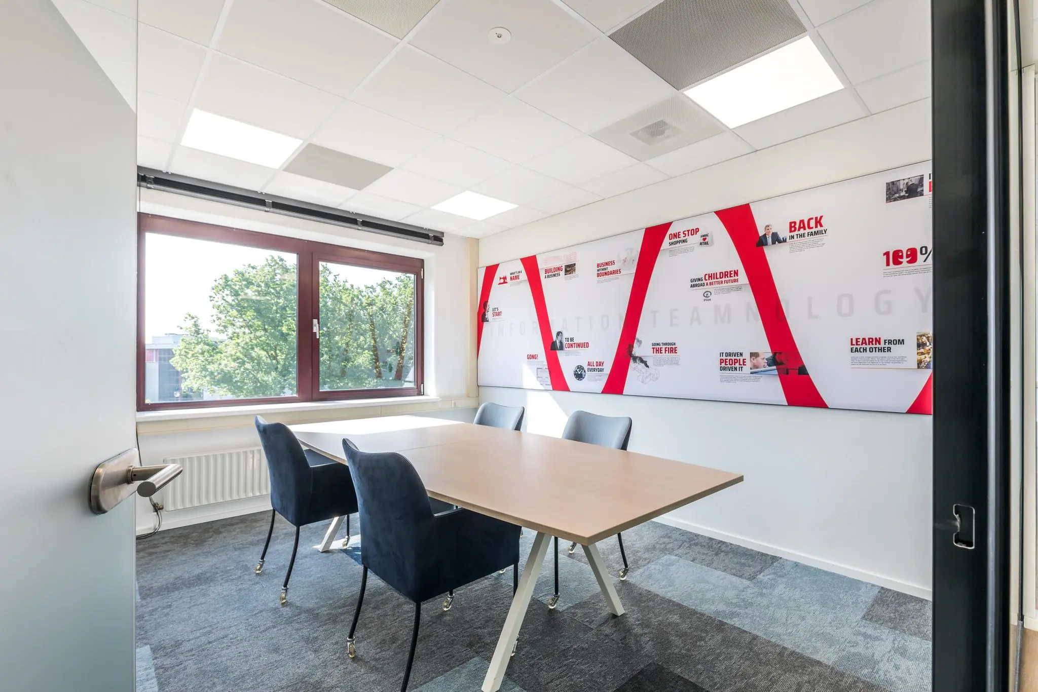 Vergaderruimte aan de Baarnsche Dijk met een houten tafel, vier stoelen en een grote inspiratiewand met rode accenten.